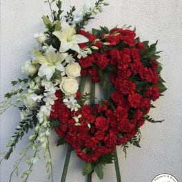 Heart-shaped floral wreath with red carnations and white lilies on an easel