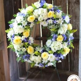 Standing wreath of yellow roses, white daisies, and purple flowers on a metal easel