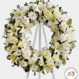 Large white funeral wreath with lilies and roses displayed on a white easel stand