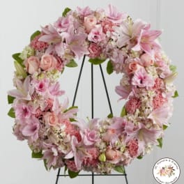 Pink and white floral wreath of lilies, roses, carnations, and hydrangeas on a black stand