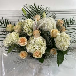 Cream roses and white hydrangeas arranged with lilies in clear wrap