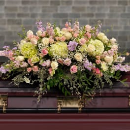 Pastel pink and cream casket spray with roses and hydrangeas on a dark wood casket