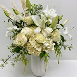 White lilies and roses arranged in a tall white vase