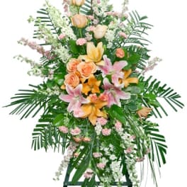 Tall standing spray with pink lilies and peach roses on a green easel
