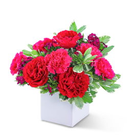 Red and pink floral arrangement in a white square vase
