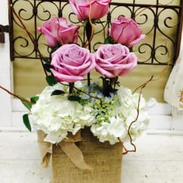 Pink roses arranged above white hydrangeas in a burlap-wrapped container