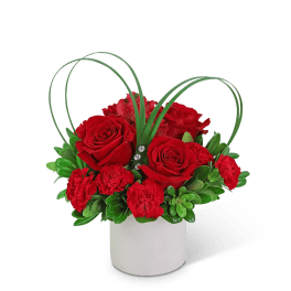 Red roses and carnations in a white vase with looping grass accents
