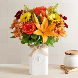 Bouquet of orange and yellow flowers in a white vase with a ribbon