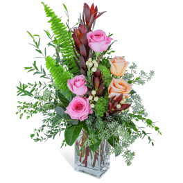 Pink and peach roses in a clear glass vase with mixed greenery