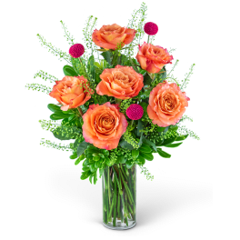 Orange roses in a clear glass vase with pink pom-pom accents