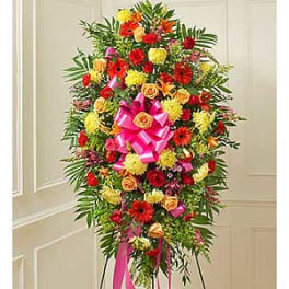 Tall standing spray of mixed red, yellow, and orange flowers with pink ribbon