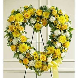Yellow and white floral wreath on a stand with a ribbon bow