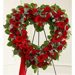 Heart-shaped red floral wreath on a black stand with a red ribbon