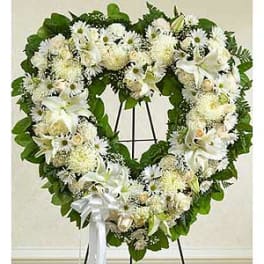 Heart-shaped white floral wreath on a stand with a white ribbon