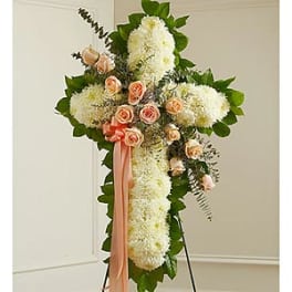 Standing floral cross with white blooms and peach roses on an easel