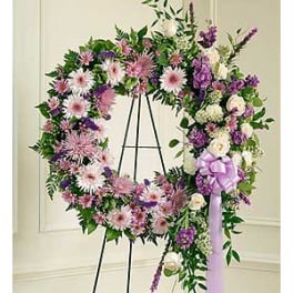 Large purple and pink floral wreath on a black stand with a lavender ribbon
