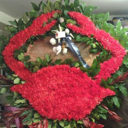 Large red floral funeral wreath with a ribbon and greenery