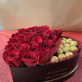 Red roses arranged in a heart-shaped box with gold-wrapped chocolates