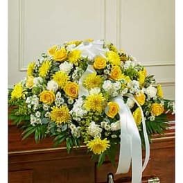 Yellow and white funeral spray with ribbon on a casket