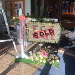 White floral standing sign with a red "SOLD" banner and pink ribbon
