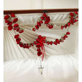 Red rose garlands draped over white fabric with a crucifix below