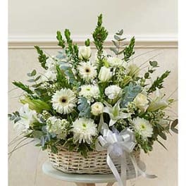 White floral arrangement in a wicker basket with a silver ribbon