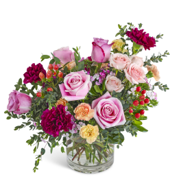 Mixed arrangement of pink roses, dark red carnations, and peach blooms in a clear glass vase