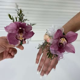 Purple orchid corsages worn on wrists with ribbon accents