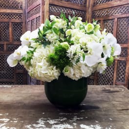 White floral arrangement in a dark vase with orchids and hydrangeas