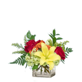 Bouquet of red roses, yellow lilies, and orange flowers in a clear square vase