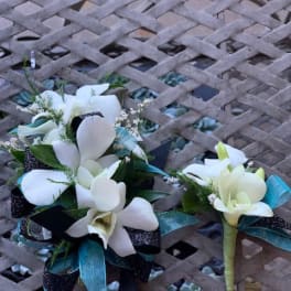 Two white floral corsages with teal ribbon accents on a lattice table