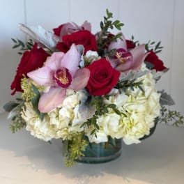 Bouquet of red roses, pink orchids, and white hydrangeas in a glass vase