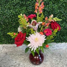 Mixed bouquet with red roses, a white daisy, and lilies in a glass vase