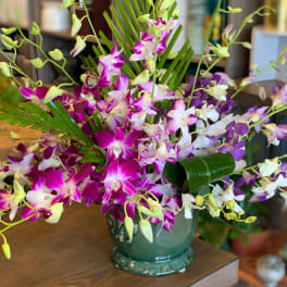 Tropical arrangement of purple and white orchids with palm fronds in a green ceramic pot