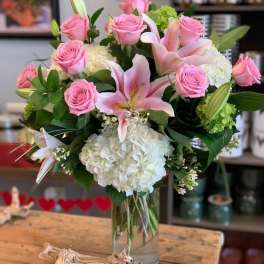 Vase arrangement of pink roses, white hydrangeas, and pink lilies in a clear glass cylinder