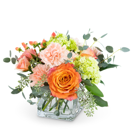 Orange roses and pink carnations in a clear square vase
