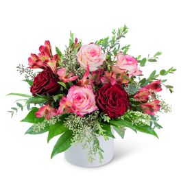 Pink and burgundy roses in a white vase with mixed greenery