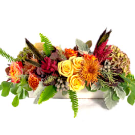 Low floral arrangement with yellow roses and orange blooms in a white container