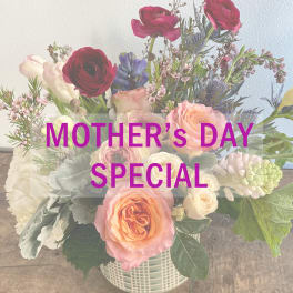 Mixed bouquet of roses, ranunculus, and pastel blooms in a white basket vase