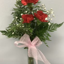 Red carnations in a glass vase with baby’s breath and a pink ribbon