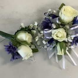 Two small floral corsages with white roses and purple flowers, tied with silver ribbon.