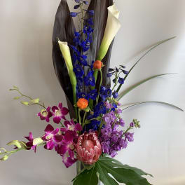 Tall mixed bouquet with blue, purple, and white blooms in a glass vase