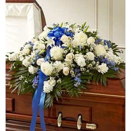 White and blue floral casket spray with a ribbon on a wooden casket