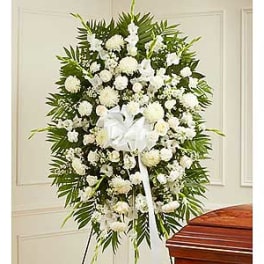 Large white funeral spray with ribbon on an easel beside a casket