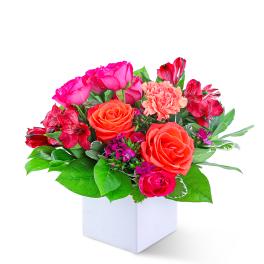 Pink and orange flower arrangement in a white cube vase