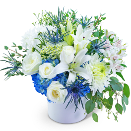 White lilies and roses in a white vase with blue hydrangea accents