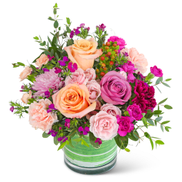 Mixed bouquet of peach, pink, and purple flowers in a green glass vase