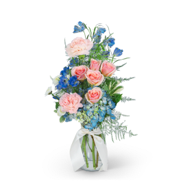 Pink roses and blue flowers in a glass vase with a white ribbon