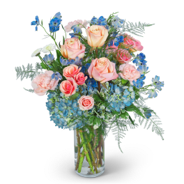 Pink roses and blue flowers arranged in a clear glass vase
