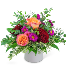 Bouquet of orange and red roses with purple daisies in a white vase